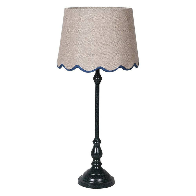 A slim very dark green, metal table lamp with a traditional design. It features a slender, ornate stand and a beige linen lampshade with a scalloped edge trimmed in blue. 