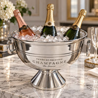 A large silver champagne bucket. The bucket has engraved text reading 'CUVÉE DE PRESTIGE 