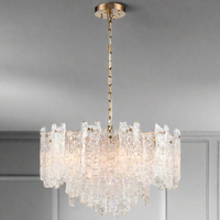 Large chandelier featuring clear textured glass shards of varying heights suspended from an aged brushed‑brass frame and chain.