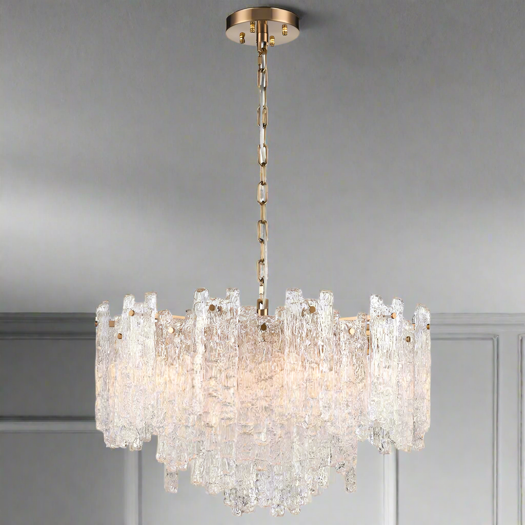 Large chandelier featuring clear textured glass shards of varying heights suspended from an aged brushed‑brass frame and chain.