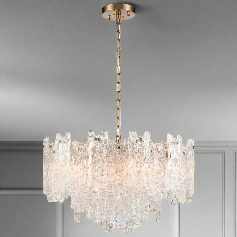 Large chandelier featuring clear textured glass shards of varying heights suspended from an aged brushed‑brass frame and chain.