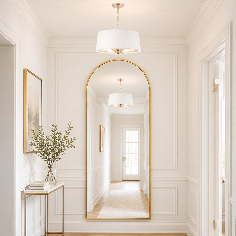Elegant interior design with a large arched mirror, white walls, and decorative white shaded, gilt metal light.