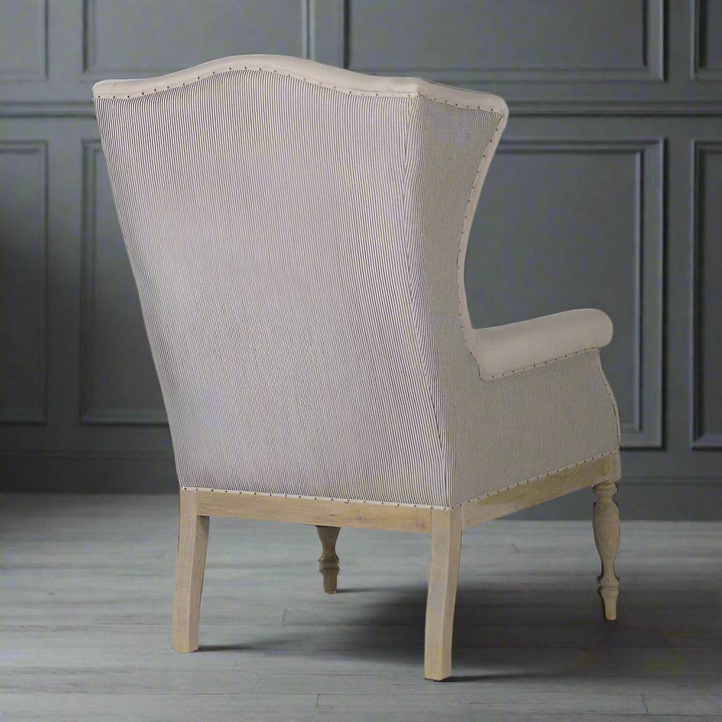 A very pared back, light coloured wing chair sitting on tapered, turned wooden legs. A very neutral armchair that would work well as a country house chair. 
