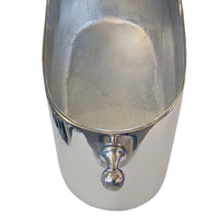 A close-up of a polished silver metal scoop or ice bucket with a rounded handle, shown against a plain white background.