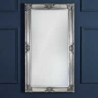 Tall, silver,  ornate rococo framed mirror against a dark plain background