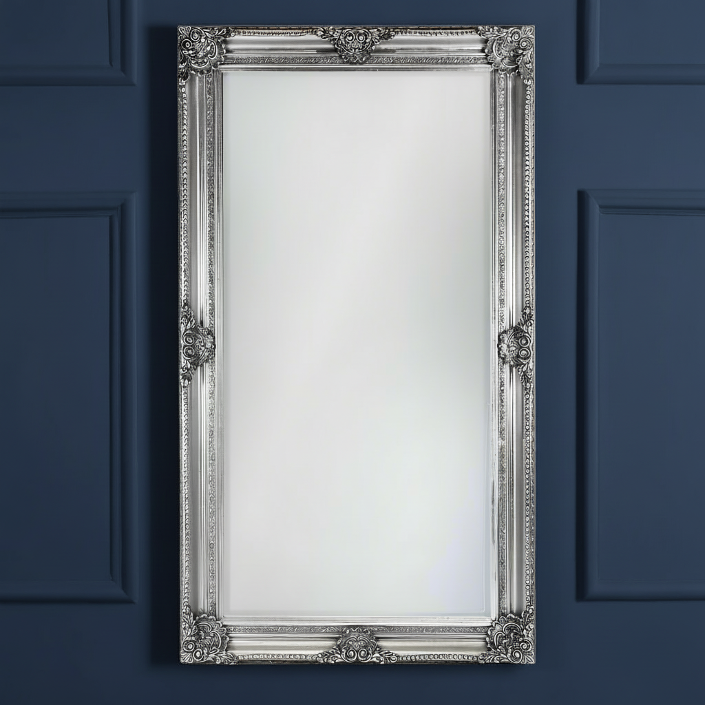 Tall, silver,  ornate rococo framed mirror against a dark plain background