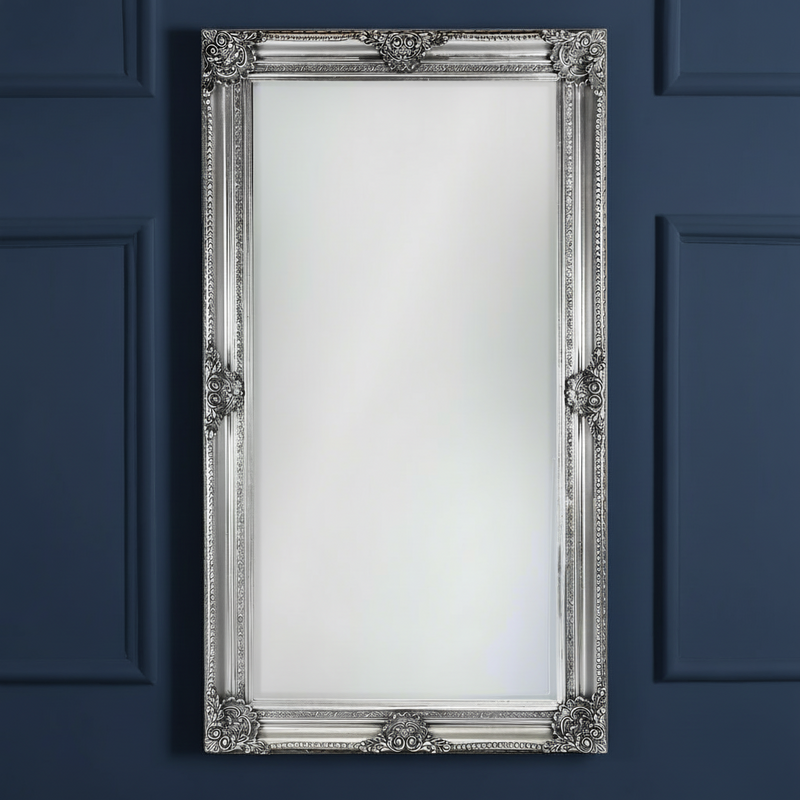 Tall, silver,  ornate rococo framed mirror against a dark plain background
