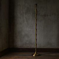 Mid-century modern floor lamp with gold tiered base and dark fabric drum shade beside a green velvet armchair.