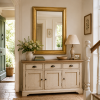 Gold framed, beaded edge wall mirror, classic style in a country cottage setting over a painted dresser near a staircase.