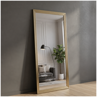 Gold-framed mirror leaning against a gray wall with a living room reflection.