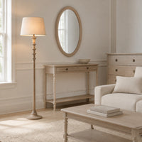 A styled living room featuring a light beige/cream console table, a matching floor lamp, a round wood-framed mirror, and a light-colored armchair.
