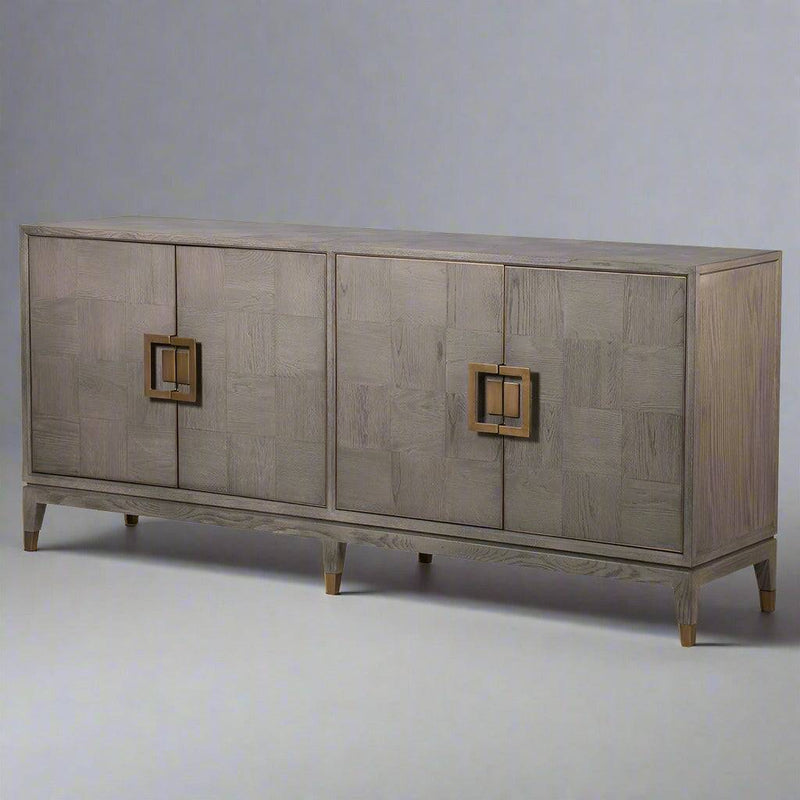 A sleek, contemporary long sideboard in a pale grey finish.&nbsp; This sideboard has four doors and has a particular stylish set of handles to the door in a dark gilt finish.&nbsp; There is a pattern of squares in the wooden surface of this piece. The sidebaord has four doors and two shelves behind each door, which provides ample storage.&nbsp; Perfect contemporary piece for your dining or living room, the colour of this sideboard would work well in a contemporary setting.