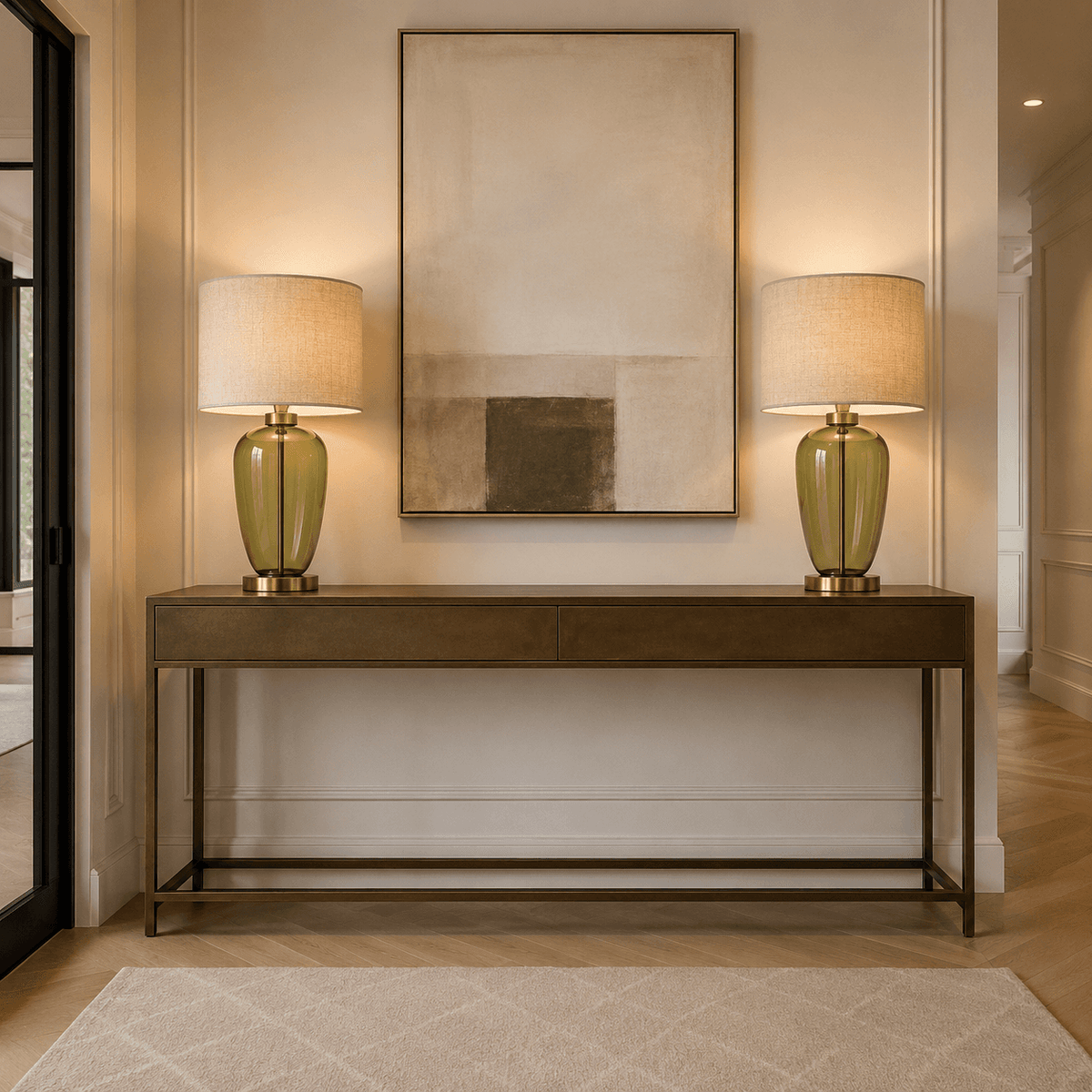 A modern console table in a warm wood finish with a black metal frame, styled in a hallway with two matching table lamps and a large abstract painting on the wall.
