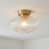 A modern semi-flush mount ceiling light fixture featuring a ribbed, clear glass shade in brushed brass.