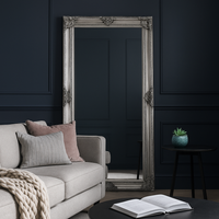 Massive, silver rococo mirror in a dark,panelled sitting room with pale furniture.
