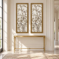 Pair of tall Chinoiserie painted mirrors in gilt rectangular frames displayed above a simple gold console table in a bright hallway.