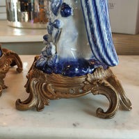 Decorative blue and white ceramic figure on a gold stand with a blurred background