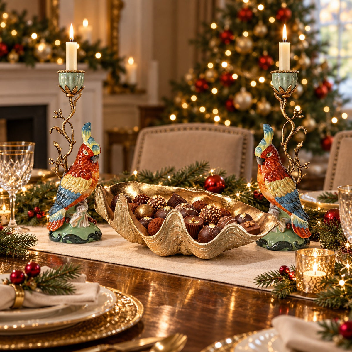 A festive Christmas table setting featuring two colorful parrot bird candlestick holders flanking a gold shell centerpiece filled with ornaments.