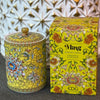 Handcrafted yellow ceramic scented candle jar with gold detailing and floral design, scented with Pineapple and Coconut.