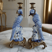Pair of blue and white ceramic parrot candle holders on a marble surface.