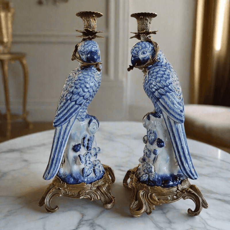 Pair of blue and white ceramic parrot candle holders on a marble surface.