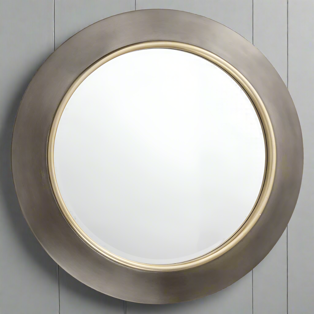 Front view of a round glass mirror with a broad gunmetal coloured resin frame and narrow gilt inner rim, shown against grey wall panelling