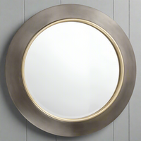 Front view of a round glass mirror with a broad gunmetal coloured resin frame and narrow gilt inner rim, shown against grey wall panelling