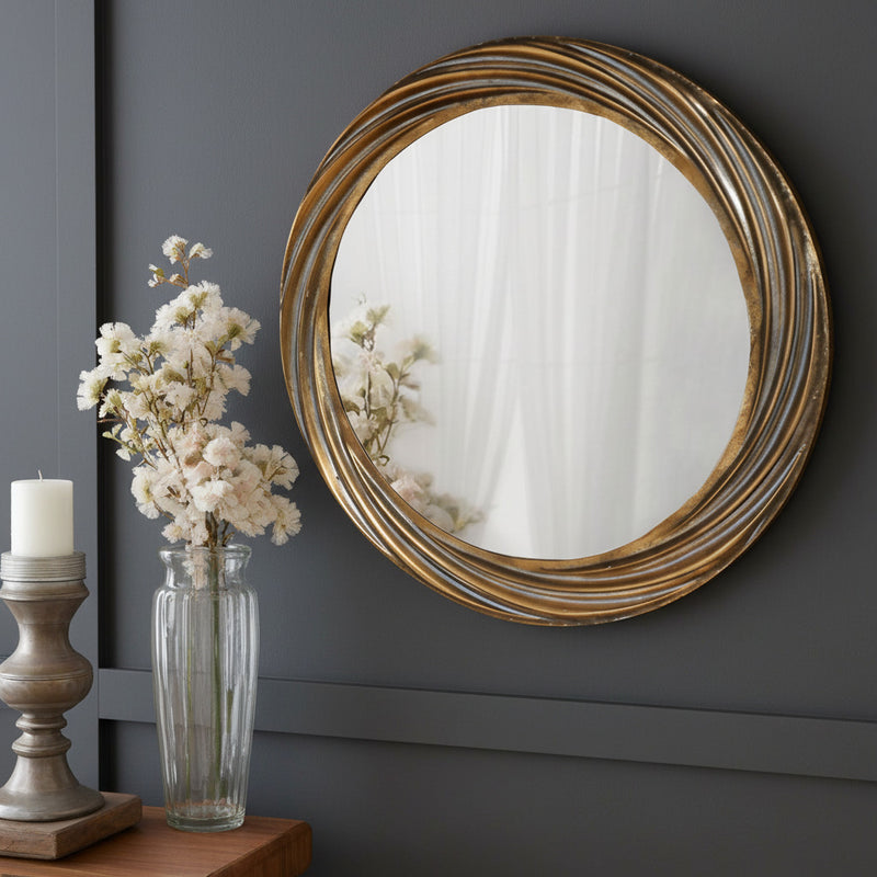 A round wall mirror with a distressed gold, deeply textured frame and a swirling pattern of the frame 