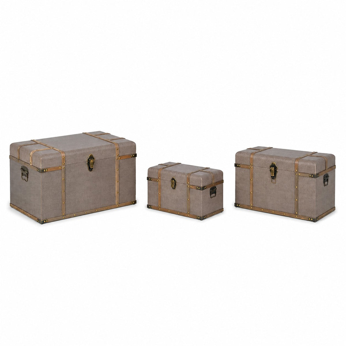 Three upholstered storage trunks in a taupe-gray fabric with brass-toned metal trim and handles, shown in three sizes on a white background.