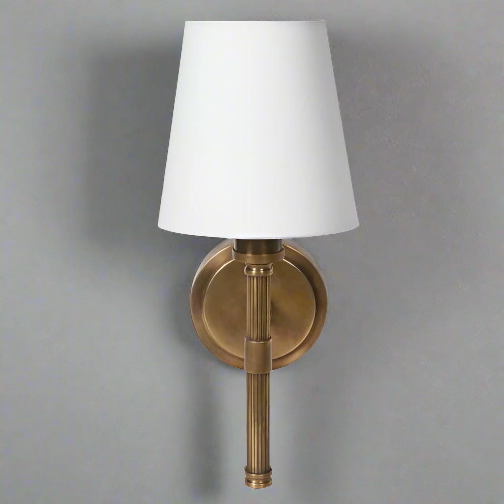 A single antique wall brass light with ribbed metal sconce and white linen shade.&nbsp; Perfect wall light for a bedroom, living room or hall.&nbsp; The antique brass finish works well in a country house or period town house interior. These wall lights are the perfect addition to any space , allowing a warm ember glow through the white linen shade to illuminate your room.&nbsp; Blending classic elegance with a warm understated vintage style, exceptional lighting for an exceptional interior.