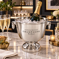 Small round polished silver champagne cooler with two decorative ring handles and a raised pedestal base on a contemporary bar.