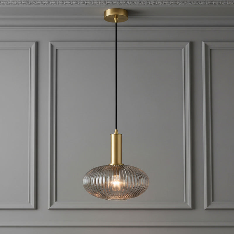 Pendant light with gold fixture and ribbed glass shade on a white background