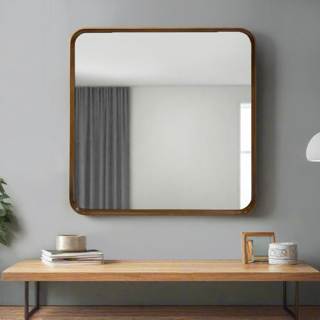 Square wall mirror with rounded walnut wood frame over a coffee table agaist a grey painted wall.