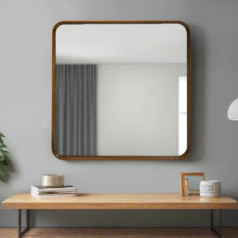 Square wall mirror with rounded walnut wood frame over a coffee table agaist a grey painted wall.