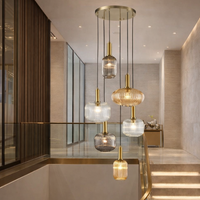 Six ribbed glass pendant hanging in a contemporary stairwell in a modern setting, with brass stairwell and pale walls.