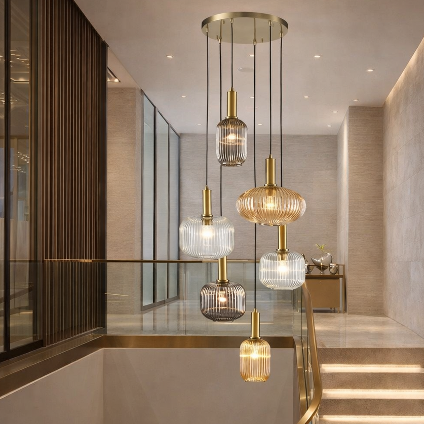 Six ribbed glass pendant hanging in a contemporary stairwell in a modern setting, with brass stairwell and pale walls.