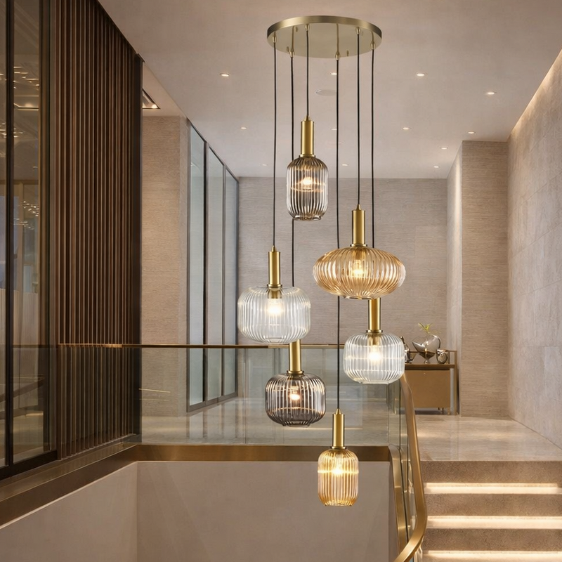 Six ribbed glass pendant hanging in a contemporary stairwell in a modern setting, with brass stairwell and pale walls.