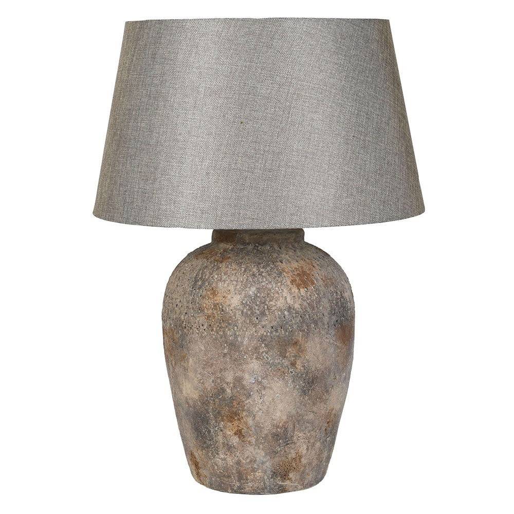 A table lamp with a textured, rustic ceramic base in earthy brown and gray tones, topped with a light gray linen drum shade, shown against a plain white background.