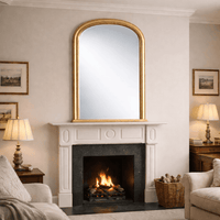 Tall gilt overmantle mirror with arched top, gold frame above fireplace in traditional country home.