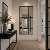 Tall black metal window mirror in a hallway reflecting the door. 