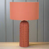 This is a ceramic table lamp finished in a warm terracotta color, featuring a monochromatic design where both the base and the drum-shaped fabric shade share the same earthy hue. The lamp base stands out with its raised bobble texture, giving it a tactile and contemporary appeal. The base is tall and cylindrical with a rounded top, and the bobbled surface adds visual depth and a handcrafted feel, while the uniform terracotta finish provides a cohesive, minimalist look. This lamp is ideal for interiors with 