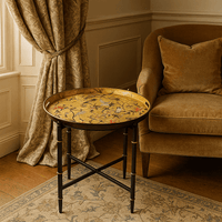 Decorative round table with floral design in a room with a brown armchair and patterned curtains.