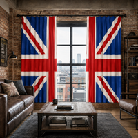 A pair of floor-length curtains featuring a large Union Jack flag design, hanging on a black rod over a tall window in a rustic loft room with brick walls, a leather sofa, and a wooden coffee table.