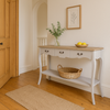  French country console table featuring a vintage white finish, natural wood top, ornate drawer handles, and a spacious lower shelf. For entryways, hallways, or living rooms.