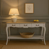  French country console table featuring a vintage white finish, natural wood top, ornate drawer handles, and a spacious lower shelf. For entryways, hallways, or living rooms.