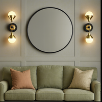 Green sofa with decorative pillows in a room with wall lights and a round mirror.