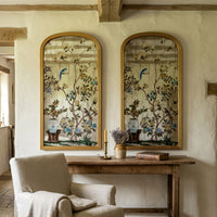 A pair of decorative arched mirrors with Victorian bird and floral detail, above a hallway console table in a country house hallway