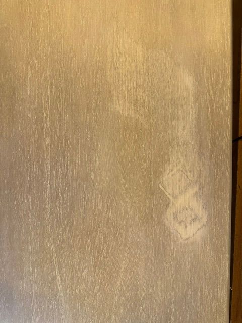 A close-up of a light beige or cream-colored textured surface with subtle vertical grain and a faint smudge or stain near the lower right area.