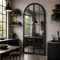 tall, grey arched window mirror in contemporary kitchen setting with dark, mid-century furniture and sink unit. 
