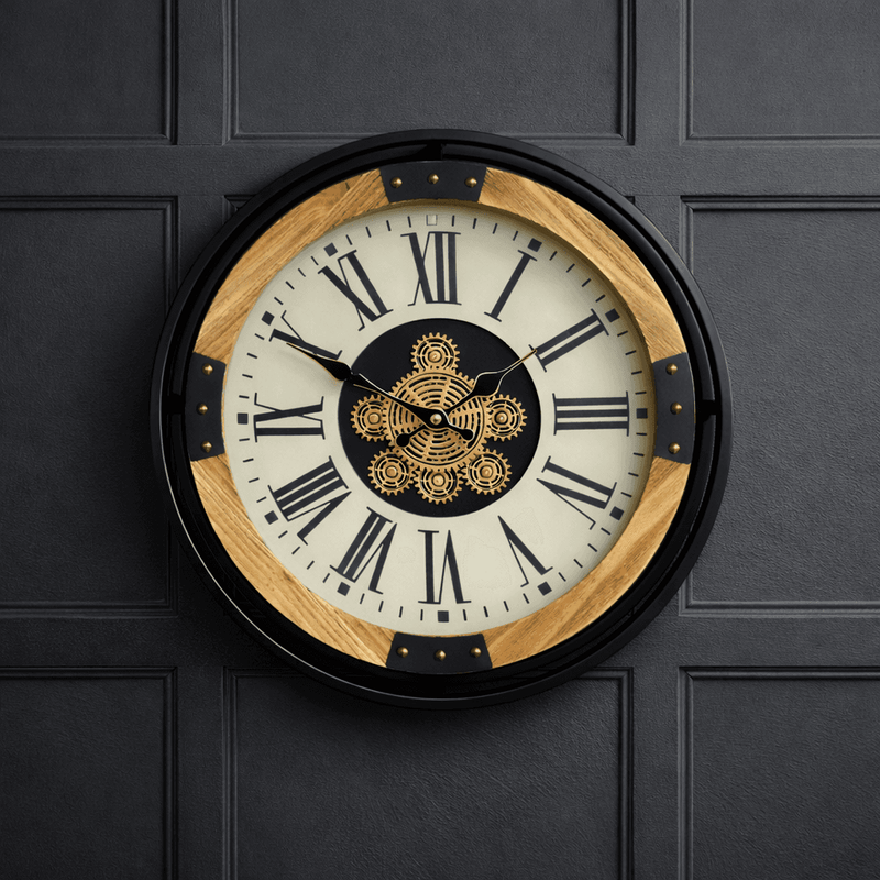 Large industrial wall clock with exposed moving gears, black metal frame, wood accents, and Roman numeral dial mounted on a dark paneled wall.